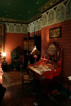 an old fashioned desk and chair in a room with red wallpaper, green ceilinging and ornately decorated walls