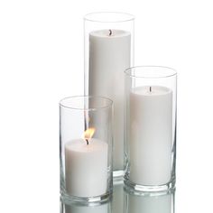 three white candles in glass vases with one lit candle on the side and another empty