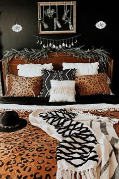 a leopard print bed spread with pillows and blankets on top of it, next to a black wall