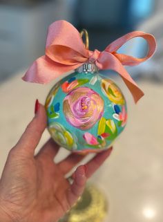 a hand holding an ornament with a pink bow on it