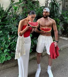 a man and woman standing next to each other holding watermelon slices