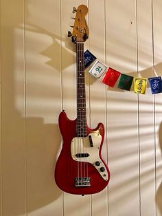 a red guitar hanging on the wall with some tags attached to it's neck