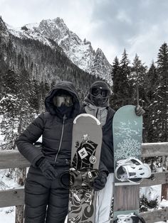 two snowboarders standing next to each other holding their boards in the snow with mountains in the background