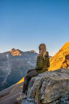 a woman sitting on top of a mountain looking at the mountains in the distance with her back to the camera