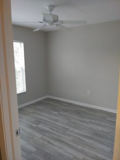 an empty living room with wood flooring and ceiling fan in it's corner