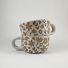 two coffee cups with floral designs on them sitting side by side in front of a white background