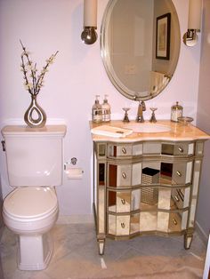 a white toilet sitting next to a bathroom sink under a round mirror on top of a wooden cabinet