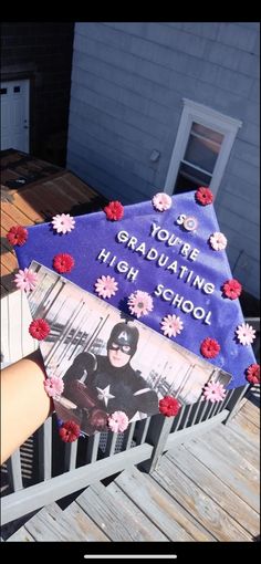 a graduation cake with flowers on it sitting on top of a wooden deck next to a building