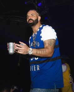 a man with a beard holding a cup in his hand and wearing a blue shirt