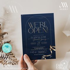 a person holding up a blue and gold wedding card with the words we're open on it