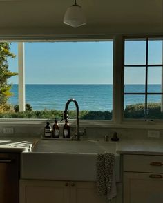 a kitchen sink sitting under two windows next to the ocean