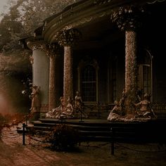 an old building with columns and statues on the front porch, surrounded by foggy trees