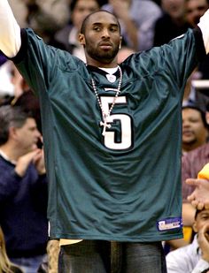 a man in a football jersey holding his hands up to the side with other people watching