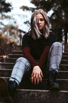 a woman is sitting on the steps in front of trees and looking at the camera