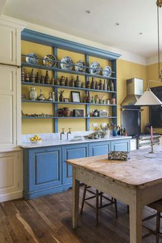 a kitchen with blue and yellow cabinets, wooden table and shelves filled with dishes on the wall