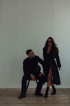 a man sitting next to a woman on a chair in front of a white wall