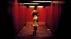 a woman walking down a long hallway with red walls