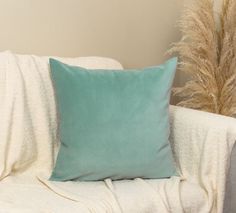 a green pillow sitting on top of a white couch next to a tall grass plant