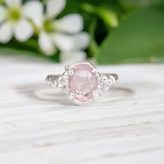 a pink diamond ring sitting on top of a wooden table next to flowers and greenery