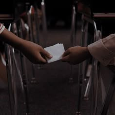 two people holding their hands over a piece of paper on a chair in a room