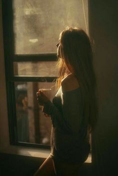 a woman standing in front of a window holding a coffee cup and looking out the window