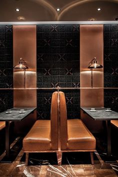 two brown chairs sitting next to each other in front of a wall with black tiles