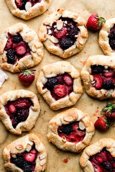 strawberry pies are arranged on a sheet of parchment paper and topped with fresh strawberries