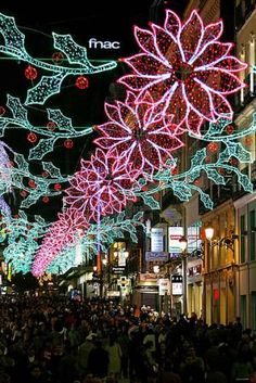 people are walking down the street decorated with christmas lights