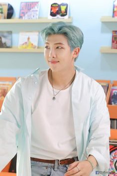 a man with blue hair standing in front of bookshelves