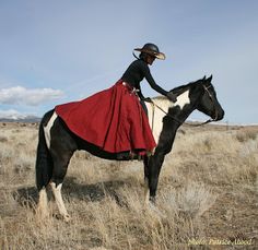 a woman in a red dress riding on the back of a black and white horse