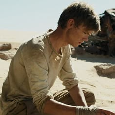 a man kneeling down in the sand next to a car