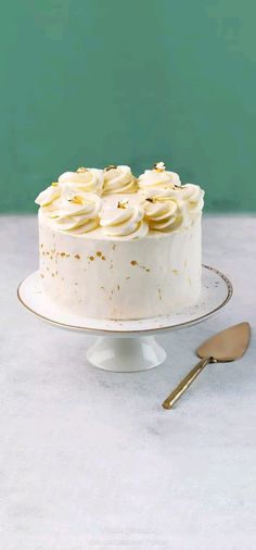 a cake with white frosting and gold decorations on a plate next to a knife