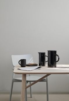 two black coffee mugs sitting on top of a wooden table next to a white chair