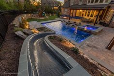 an outdoor swimming pool surrounded by landscaping and trees at dusk with lights on in the background