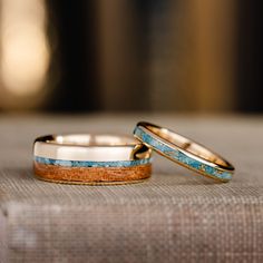 two gold wedding bands with blue and brown wood inlays are sitting on a piece of cloth