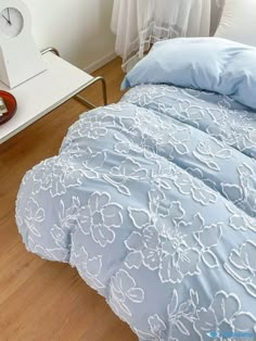 a blue comforter with white flowers on it next to a nightstand and clock in the corner