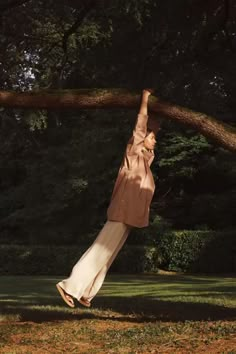 a woman is hanging upside down on a tree branch in the park with her arms outstretched