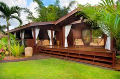 a wooden house sitting on top of a lush green field next to trees and bushes