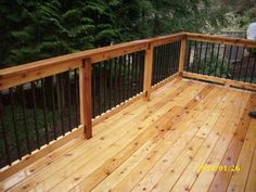 a wooden deck with metal railings and trees in the backgroung area