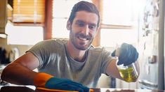 a man is smiling while cleaning the kitchen counter top with gloves on his hands and holding a bottle in one hand