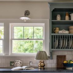 an open book is sitting on the kitchen counter next to a lamp and disheshelf