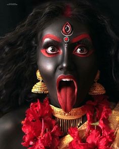 a woman with black face paint and red flowers around her neck is making a funny face