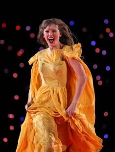 a woman in a yellow dress is on stage with her mouth open and eyes closed