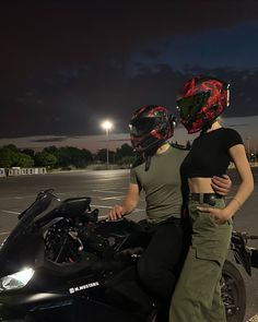 two people standing next to each other near a parked motorcycle at night with the lights on