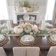 a dining room table set for thanksgiving with white pumpkins and greenery on it