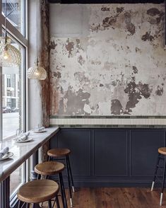 an empty restaurant with wooden stools in front of the counter and wall that has peeling paint on it