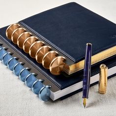 a blue notebook with gold spirals and a fountain pen on the cover next to it