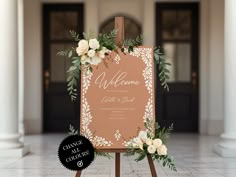 a welcome sign with white flowers and greenery on an easel in front of a building