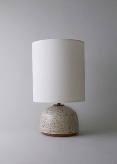 a white table lamp sitting on top of a wooden base next to a white wall