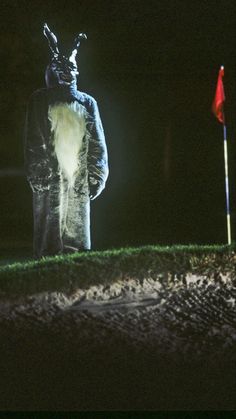 a man dressed as a rabbit standing next to a red flag on a green field